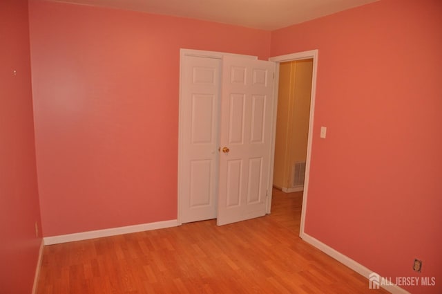 empty room with light wood-type flooring, visible vents, and baseboards