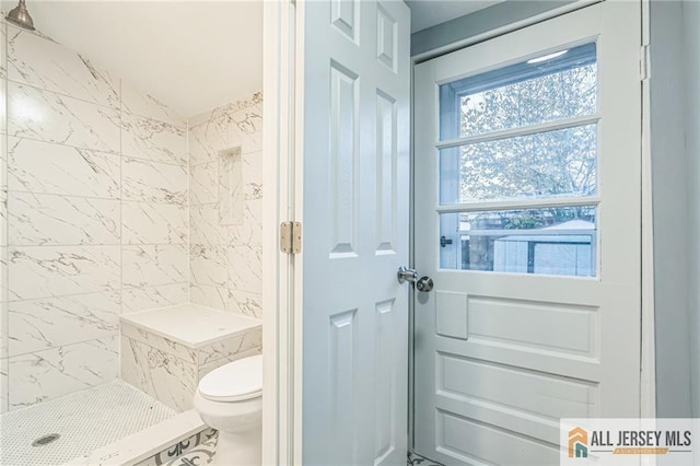 bathroom with a tile shower and toilet