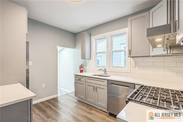 kitchen with sink, stainless steel dishwasher, decorative backsplash, gray cabinets, and hardwood / wood-style flooring