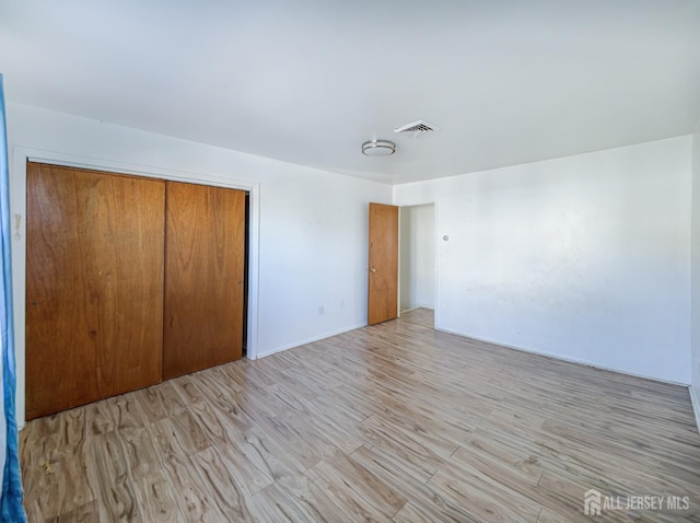 unfurnished bedroom featuring visible vents, light wood-style floors, and a closet