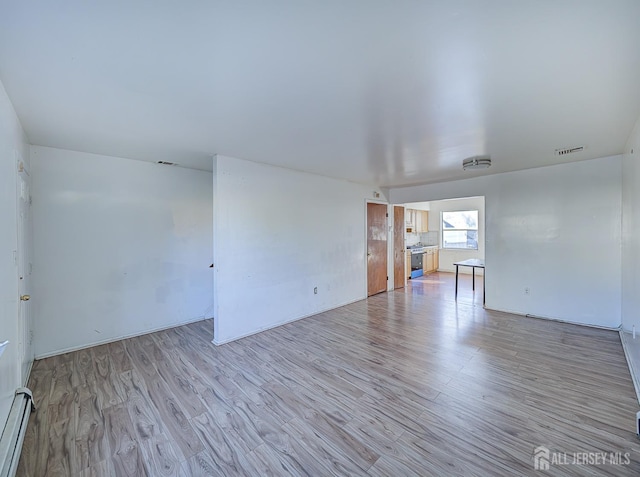 empty room with light wood finished floors, visible vents, and a baseboard heating unit