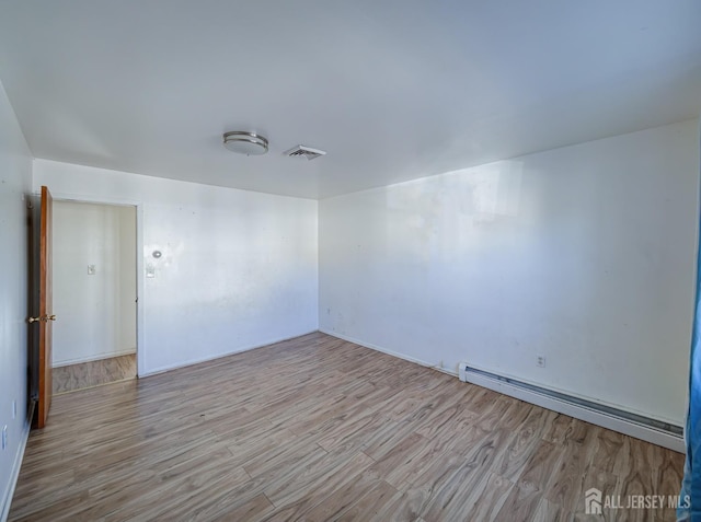 unfurnished room with a baseboard heating unit, visible vents, and wood finished floors