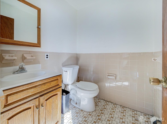 half bathroom featuring tile patterned flooring, toilet, a wainscoted wall, vanity, and tile walls