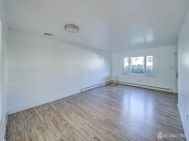 empty room with baseboards, a baseboard heating unit, wood finished floors, and visible vents