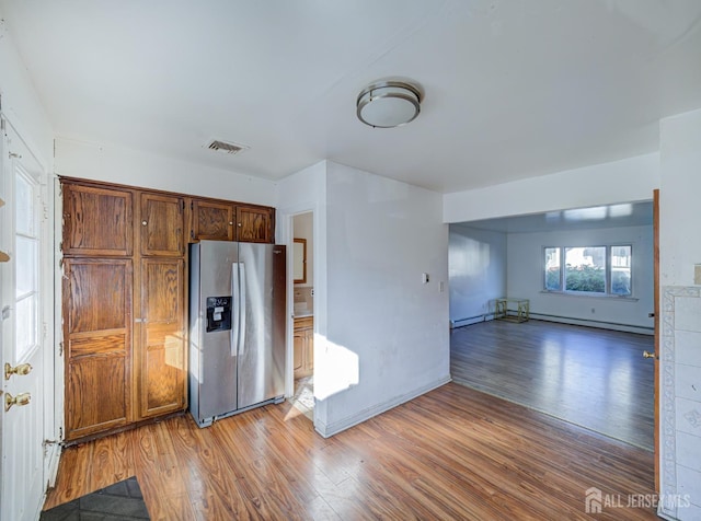 kitchen featuring visible vents, stainless steel fridge with ice dispenser, a baseboard radiator, light wood-style flooring, and open floor plan