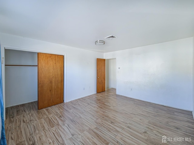 unfurnished bedroom featuring light wood-style floors, visible vents, and a closet