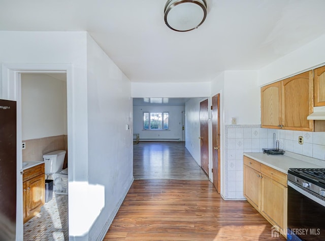 kitchen featuring stainless steel gas range oven, under cabinet range hood, wood finished floors, light countertops, and light brown cabinetry