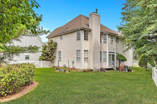 rear view of house featuring entry steps, a fenced backyard, a yard, and a chimney