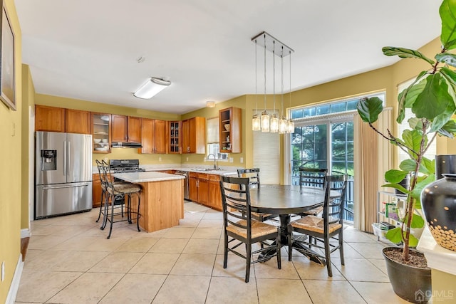 kitchen with glass insert cabinets, appliances with stainless steel finishes, brown cabinets, light countertops, and a sink