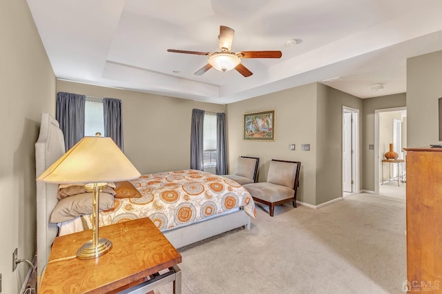 bedroom featuring multiple windows, light carpet, ceiling fan, and a tray ceiling