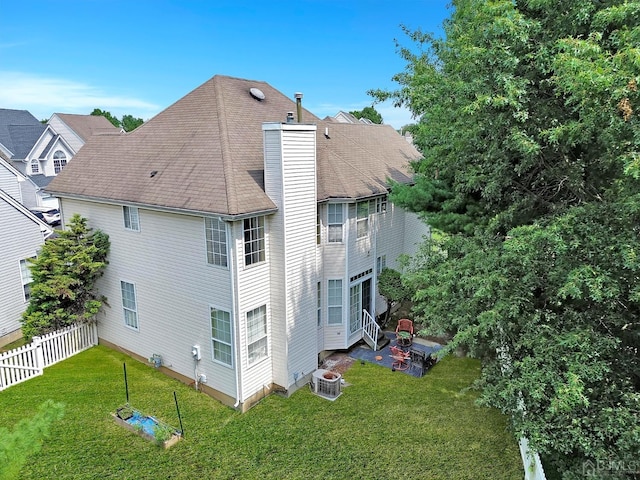 back of house featuring a lawn, a chimney, roof with shingles, fence, and central AC