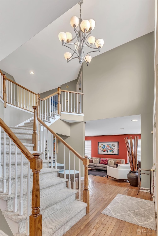 staircase featuring wood-type flooring, high vaulted ceiling, and a chandelier