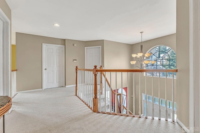 hall with a chandelier, baseboards, carpet floors, and an upstairs landing