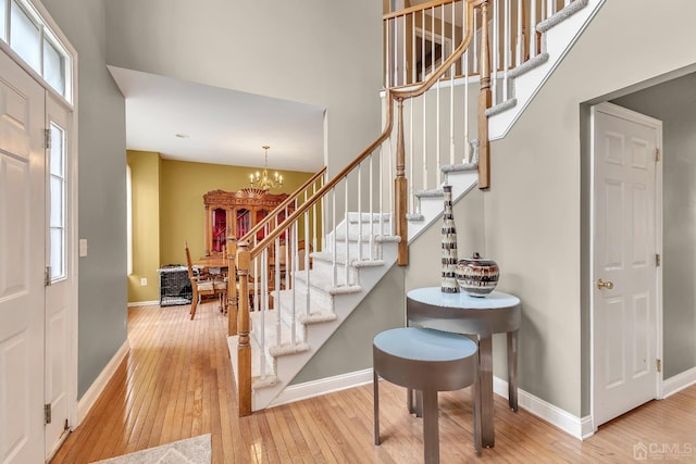 entrance foyer with stairs, a notable chandelier, baseboards, and hardwood / wood-style flooring