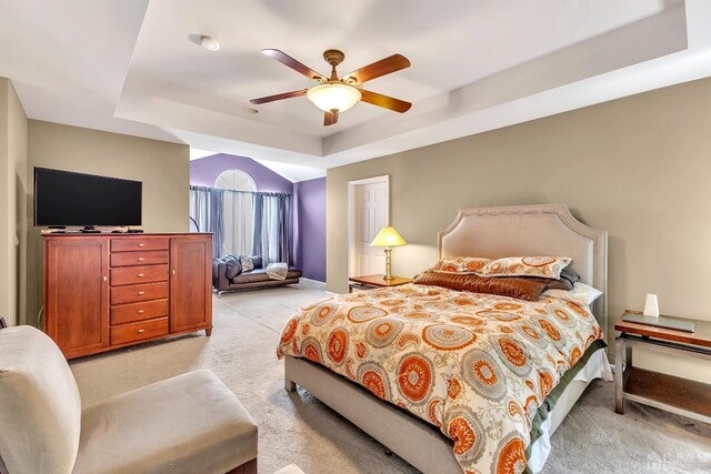 bedroom with light carpet, ceiling fan, and a tray ceiling