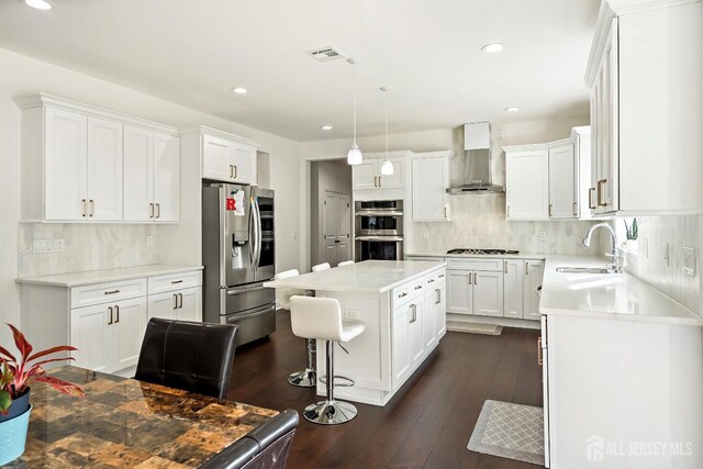 kitchen with white cabinetry, stainless steel appliances, a center island, and wall chimney exhaust hood