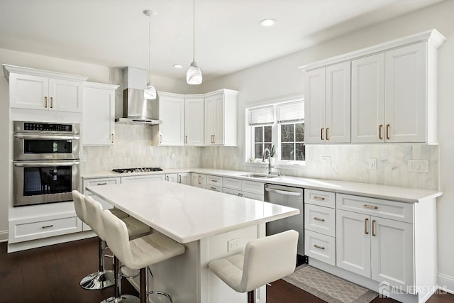 kitchen featuring sink, hanging light fixtures, white cabinets, stainless steel appliances, and wall chimney range hood