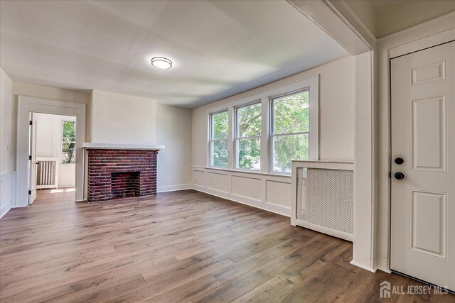 160 Academy St, South Orange Village, NJ 07079 - unfurnished living room with plenty of natural light, wood finished floors, a decorative wall, a brick fireplace, and radiator