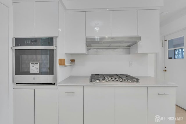 kitchen featuring under cabinet range hood, light countertops, white cabinetry, and appliances with stainless steel finishes