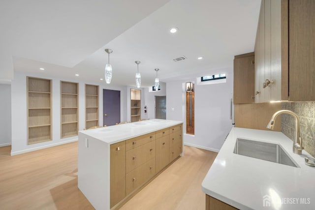 kitchen featuring visible vents, a center island, a sink, light wood finished floors, and decorative backsplash
