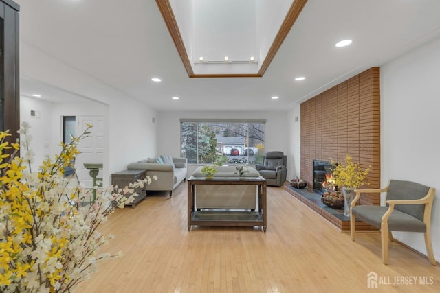 living area with a raised ceiling, light wood-style floors, a fireplace, and recessed lighting