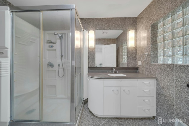 bathroom with a stall shower, vanity, granite finish floor, and tile walls