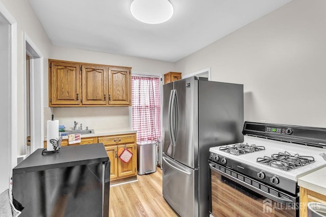 kitchen featuring light wood finished floors, light countertops, range with gas stovetop, freestanding refrigerator, and brown cabinetry