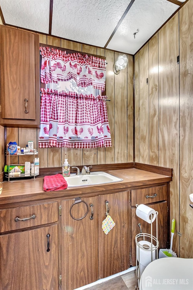 half bath with a textured ceiling, wood walls, vanity, and toilet