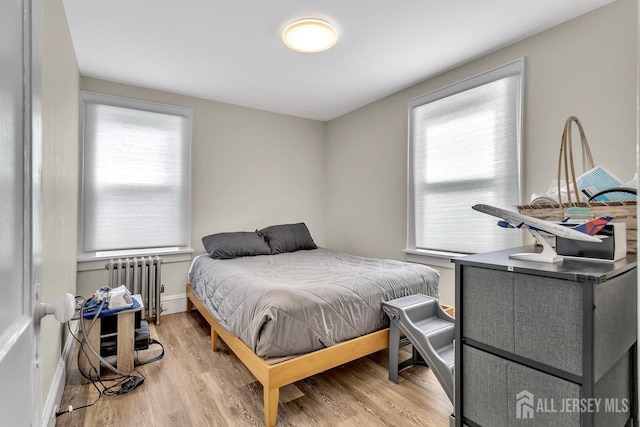 bedroom with light wood-type flooring, multiple windows, baseboards, and radiator heating unit