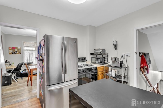 kitchen featuring range with gas stovetop, light wood-style flooring, black microwave, and freestanding refrigerator