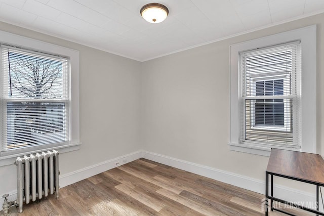 unfurnished room with radiator heating unit, light wood-style floors, baseboards, and ornamental molding