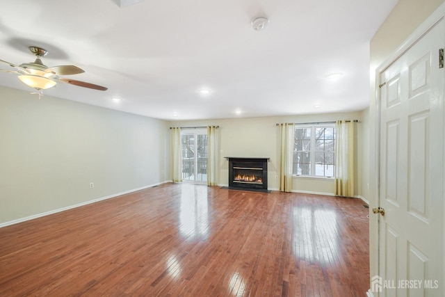 unfurnished living room with a glass covered fireplace, wood-type flooring, a healthy amount of sunlight, and ceiling fan