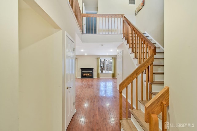 interior space with a warm lit fireplace, light wood-style flooring, a high ceiling, baseboards, and stairs