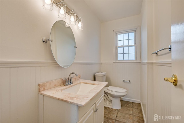 half bathroom featuring vanity, toilet, and a wainscoted wall