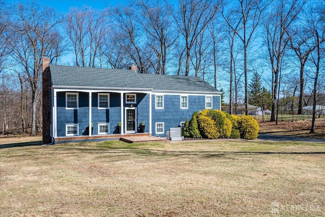 split foyer home featuring roof with shingles, a front lawn, and a chimney