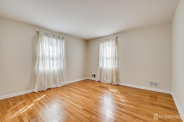 spare room featuring a wealth of natural light, visible vents, light wood-style flooring, and baseboards