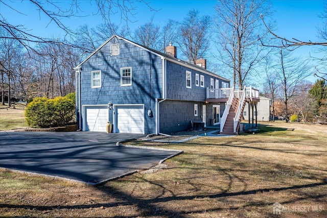 back of house featuring aphalt driveway, stairs, an attached garage, a deck, and a chimney