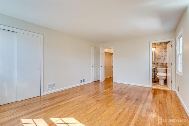 unfurnished bedroom featuring light wood finished floors, connected bathroom, baseboards, and visible vents