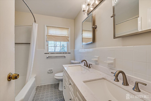 bathroom with toilet, tile walls, a wainscoted wall, and a sink