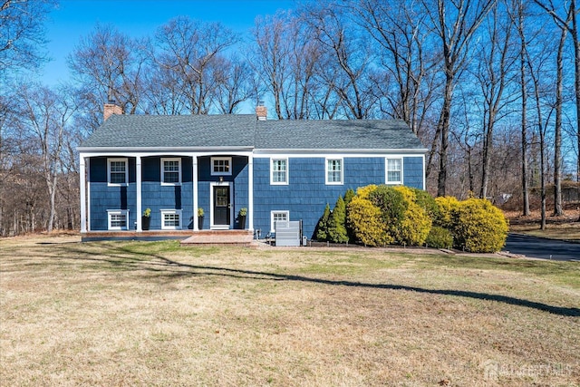 view of front facade featuring a chimney, a front yard, and a shingled roof