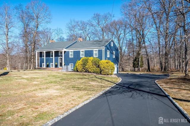 view of side of property with a chimney, driveway, roof with shingles, and a yard