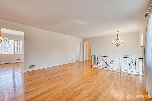 spare room featuring light wood-style floors, a chandelier, baseboards, and visible vents