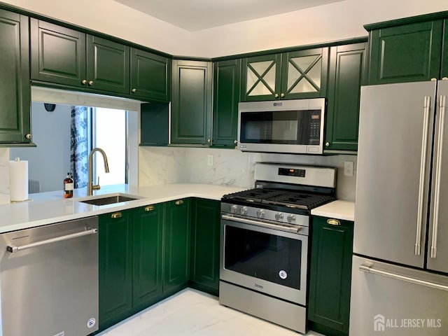 kitchen with green cabinetry, a sink, decorative backsplash, light countertops, and stainless steel appliances