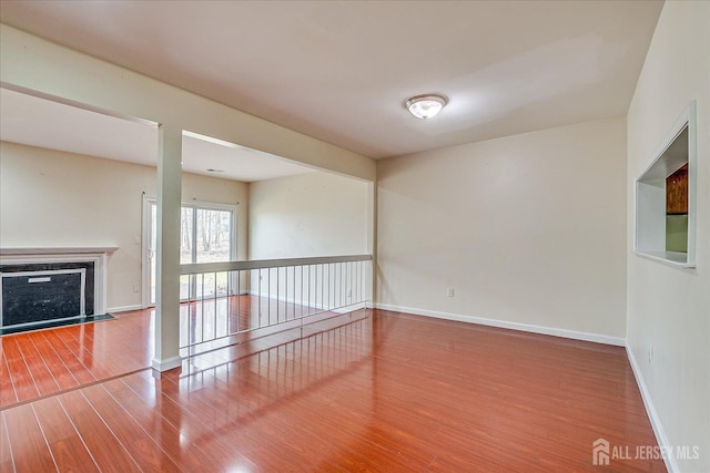 unfurnished room featuring a glass covered fireplace, wood finished floors, and baseboards