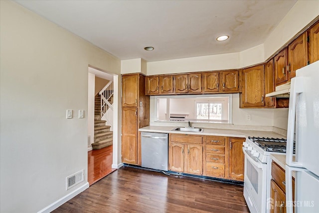 kitchen featuring under cabinet range hood, white appliances, a sink, light countertops, and brown cabinetry