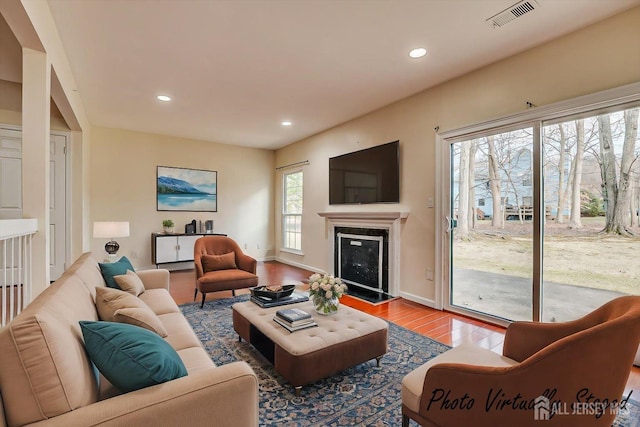 living room with recessed lighting, wood finished floors, visible vents, baseboards, and a glass covered fireplace