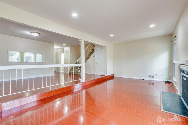 unfurnished living room with recessed lighting, visible vents, a glass covered fireplace, wood finished floors, and stairs