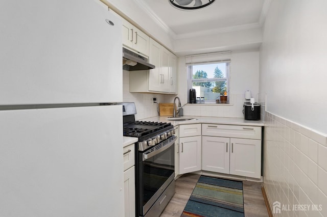 kitchen featuring under cabinet range hood, a sink, freestanding refrigerator, stainless steel range with gas stovetop, and crown molding