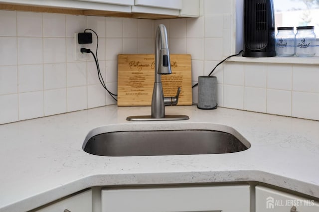 interior details featuring tasteful backsplash, a sink, and white cabinets