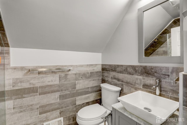 bathroom featuring visible vents, toilet, vanity, lofted ceiling, and tile walls